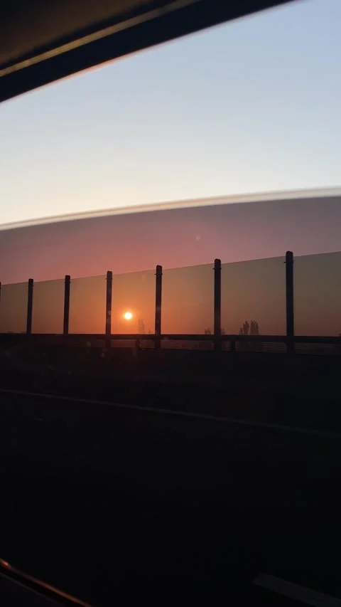 Sunset glow through car window over highway sound barrier in urban commute post Stock Footage 341662772