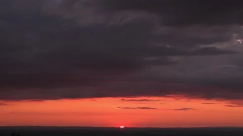 Sunset glow under heavy storm clouds, low sun dipping below horizon, deep red 스톡 동영상 323575230