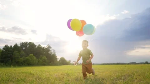Sunset glow warms sky as boy holds colorful balloons aloft. Golden light spreads Vidéo 345829879