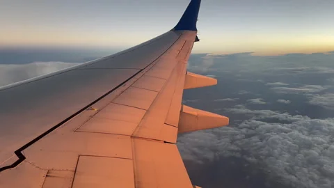 Sunset glow on the wing of a plane with clouds below Stock Footage 346878553