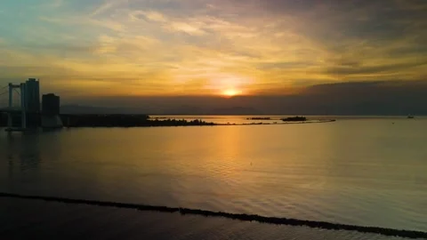 Sunset glowing over tranquil ocean waters, distant city skyline silhouetted Stock Footage 300244429