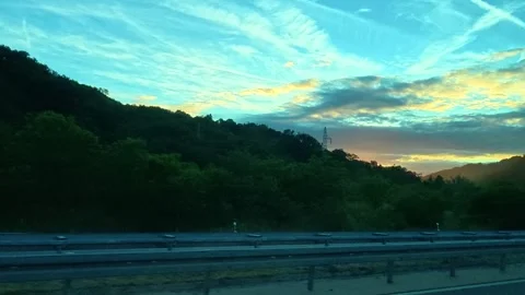 Sunset glows over forested hills beside highway. Serbia Stock Footage 340638953