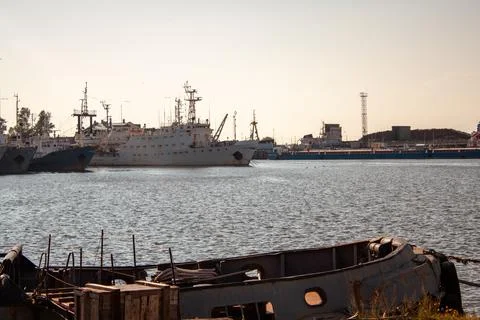 Sunset glows over harbor with large ships anchored. Broken boat rests in Stock Photos