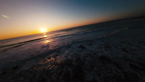 Sunset glows over ocean, waves gently crash on dark shore Stock Footage 339789101