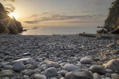 Sunset golden light over tranquil pebble beach cove Stock Photos