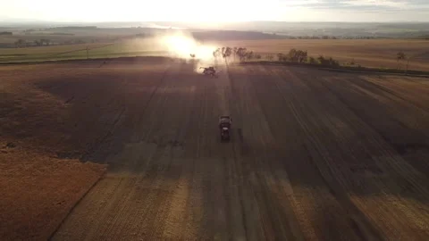 Sunset harvest combine with dust trail and red tractor pulling grain cart. Stock Footage 274658646