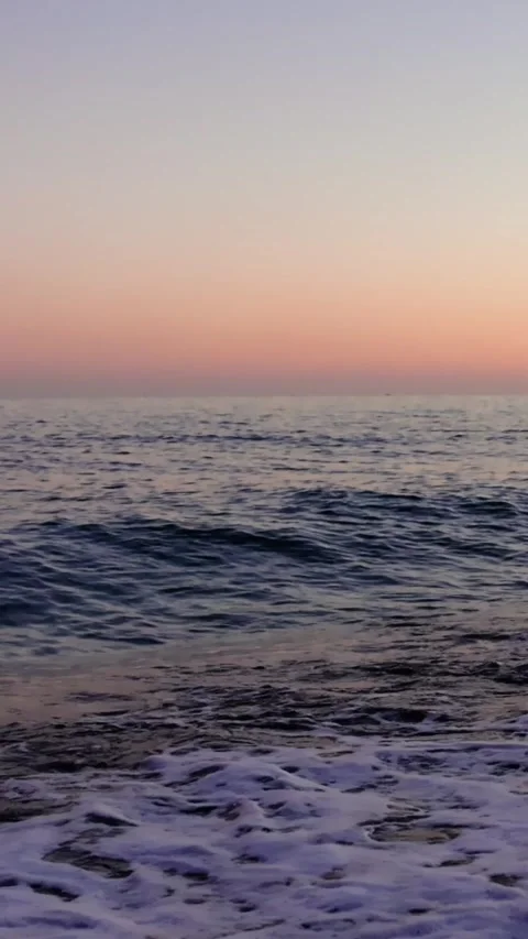 Sunset illuminates sea surf, waves gently reaching sandy beach. Waves roll onto Stock Footage 261074280