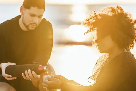 Sunset illuminating a man serving tea to a women sitting on the beach Stock Photos