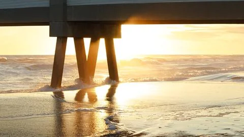 Sunset illuminating ocean waves beneath wooden pier, creating a serene Stock Photos