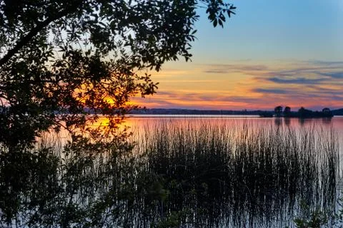 Sunset on the lake, crimson sky, blue water, reeds Stock Photos