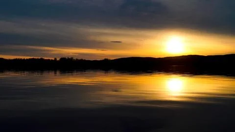 Sunset on the lake with a mirror image of the sun and sky on the water. Stock Photos