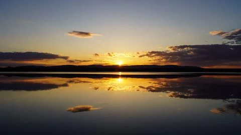 Sunset on the lake with a mirror image of the sun and sky on the water. Stock Photos