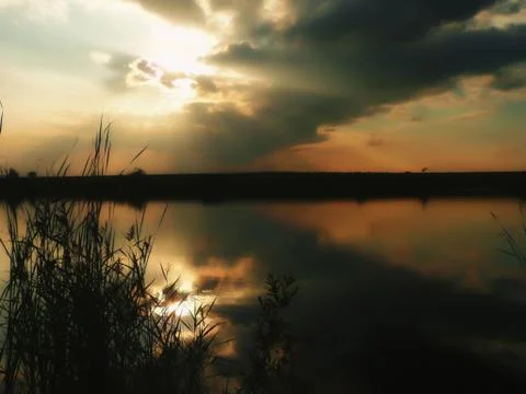 Sunset at lake, thunderclouds and grass on a shore Stockfoto's