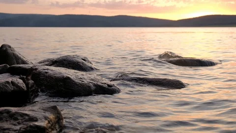 Sunset on the lake. Water beating on stones at sunset time. Stock Footage 114165553