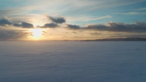 Sunset on the lake, where a strong wind is driving snow across the snow cover. Stock Footage 299795726