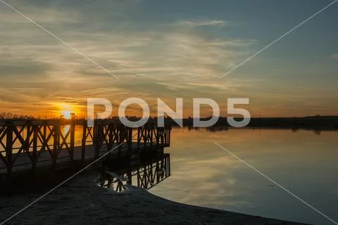 Sunset at the lake, wooden jetty on the shore Stock Photos
