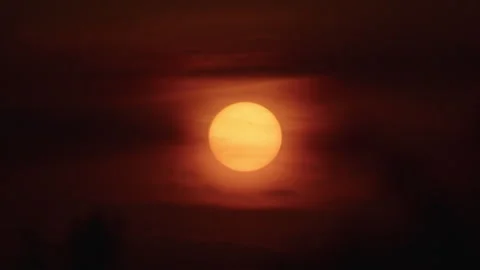 Sunset with a large orange sun partially obscured by dark clouds in the sky Stock Footage 287899444