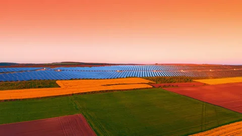 Sunset light casting warm glow on solar farm amid crop fields. Patchwork of Stockbeeldmateriaal 336899821