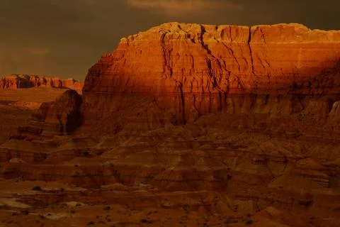 Sunset light casts shadows on rock formations in desert landscape Stock Photos