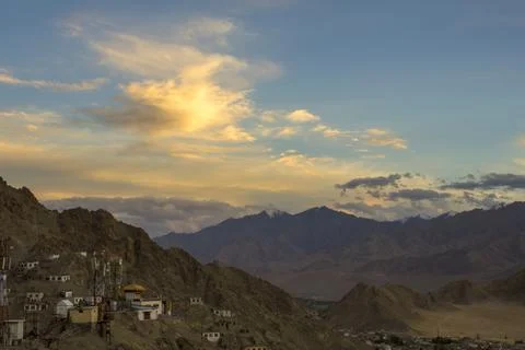 Sunset light in the clouds in the dark blue sky above the village in the mou Stock Photos