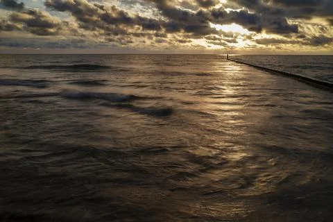 Sunset light falls across waves beside a coastal pier Stock Photos