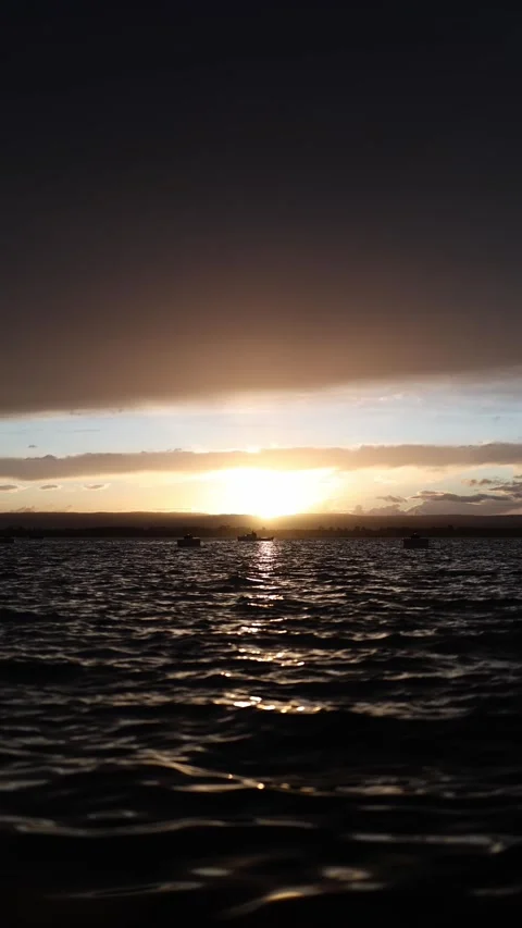 Sunset light over dark water with boats on horizon calm evening mood sky Stock Footage 327924421