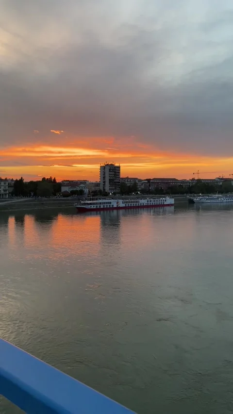 Sunset light over river with city skyline, boats, blue railing in the foreground Stock Footage 339480174