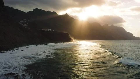 Sunset light reflected on surface oc ocean waves. Rocky shore and mountain range Stock Photos