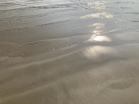Sunset light reflects on the smooth sandy beach with gentle sea waves Stock Photos