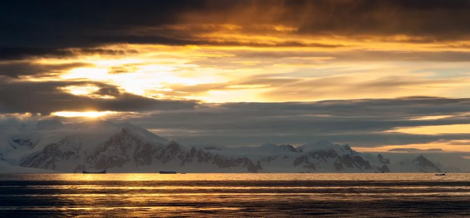 Sunset light through clouds over snow covered mountains, Antarctica Stock Photos
