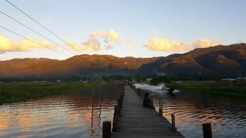 Sunset at Maing Thauk Bridge,hills in background, engine boat passes, Inle Lake 스톡 동영상 79974335