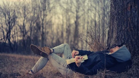 At sunset, a man lies under an oak tree and plays the guitar Stockbeeldmateriaal 90111281