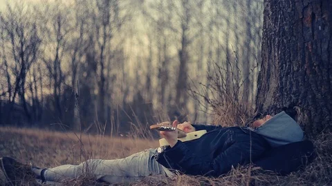 At sunset, a man lies under an oak tree and plays the guitar Stock Footage 90334765