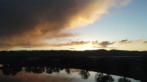 Sunset in mountains shown in lake - Drone camera moves backwards, down, &amp; right Stock Footage 137859894
