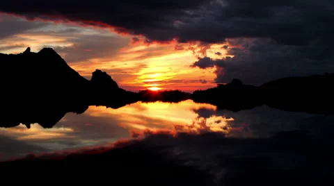 Sunset in the mountains, sun peeking out from clouds and reflected in the lake Stock Footage 61102700