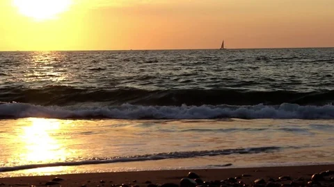 Sunset, ocean, sail boat, waves close to camera Stock Footage