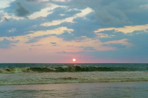 Sunset on the ocean with waves and cloudy sky Stock Photos