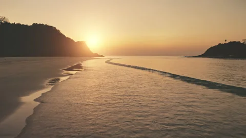 Sunset at ocean waves wash sand beach. Aerial sun set over mountain silhouette Stock Footage 143882361