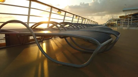 Sunset on the open ocean shining on chairs lining the deck of a cruise ship. Stockbeeldmateriaal 118667015