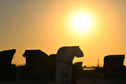 Sunset over beach chairs lined on the shore with silhouettes and golden light Stock Photos
