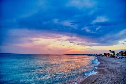 Sunset over the beach with clouds and waves at coastal location in the even.. Stock Photos