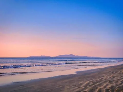 Sunset over the beach with gentle waves and distant islands in the backgrou.. Stock Photos