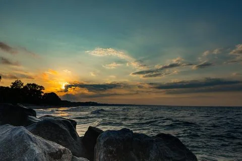 Sunset over the beach with rocks lining the shore near the water during the.. Stock Photos