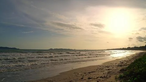 Sunset over a beach with waves and cloudy sky Stock Photos