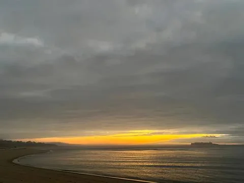Sunset over a calm beach with cloudy sky and gentle waves Stock Photos