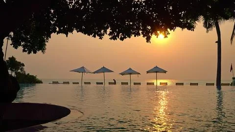 Sunset over calm beach with umbrellas and trees Stock Photos