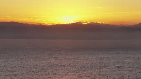 Sunset over calm ocean with distant mountain horizon Видео 337302214