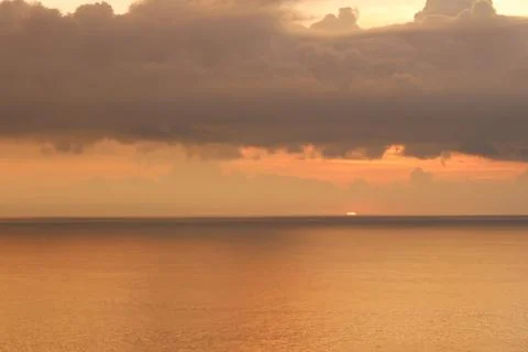 Sunset Over Calm Ocean with Dramatic Storm Clouds and Golden Light 스톡 사진