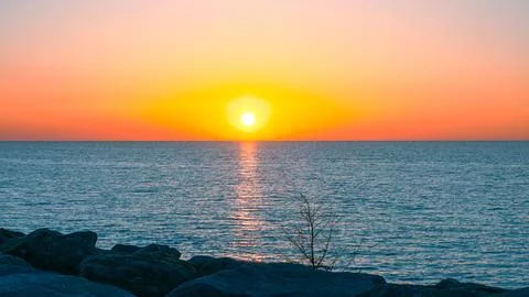 Sunset over calm ocean with rocks in foreground and vibrant sky colors Stock Photos