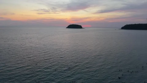 Sunset over calm ocean waters with silhouetted island and distant swimmers Видео 340406991